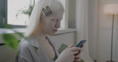 Kaygısız albino kadın sosyal medyada akıllı telefon mesajları kullanıyor sabahları yatakta dinleniyor. Gadget ve modern yaşam tarzı konsepti.