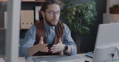 Genç adam bilgisayar ve kablosuz kulaklıkla online video görüşmesi yapıyor. Ofiste iş konuşuyorlar. Sanal toplantı ve iletişim konsepti.