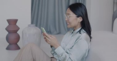 Akıllı telefon kullanan Asyalı kadının sosyal medyanın tadını çıkarması ve lüks bir dairede kahkahalar atması. İnternet iletişimi ve insan kavramı.