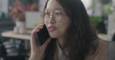 Genç Asyalı kadın çalışan cep telefonuyla ofiste iş birliği hakkında konuşuyor. İş adamları ve mesleki işgal kavramı.