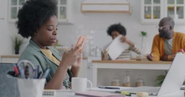 Genç Afro-Amerikalı kadın, çocuk eve geldiğinde akıllı telefon kullanıyor. Annesine sarıldığını gösteriyor. Babam arka planda oturuyor..