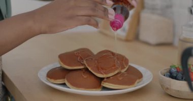 Kreplerin üzerine akçaağaç pekmezi döken ve mutfakta böğürtlenlerle süsleyen kadın elinin yakın çekimi. Sağlıklı organik gıda ve lezzetli kahvaltı konsepti.
