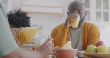 Neşeli Afro-Amerikan ailesi portakal suyunu bardağa dolduruyor mutfakta kahvaltıda lezzetli içkinin tadını çıkarıyorlar. İnsanlar ve sağlıklı beslenme konsepti.