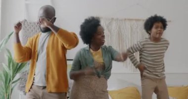 Afro-Amerikalı neşeli bir aile yatakta zıplayarak dans ediyor evdeki yatak odasında eğleniyor. Eğlence ve eğlence etkinliği konsepti.