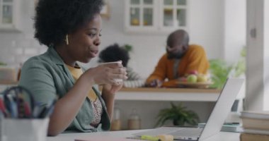 Kaygısız Afro-Amerikalı kadın internette bilgisayar ve kulaklıkla konuşuyor. Bu sırada evdeki çocukla meşgul olan adam konuşuyor. Sanal toplantı ve aile yaşam tarzı konsepti.