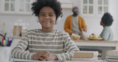 İnternette video dersi alan Afrikalı Amerikalı çocuk portresi ebeveynler mutfakta konuşurken e-öğrenmeye odaklanmış. Uzaklık eğitimi ve çocukluk kavramı.