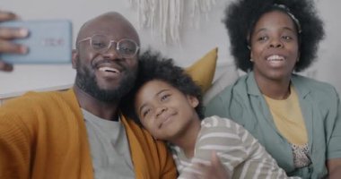 Afrikalı Amerikalılar, anne ve baba, evdeki yatak odasında akıllı telefonlarıyla çevrimiçi video görüşmesi yapıyorlar. Sanal toplantı ve aile iletişim konsepti.