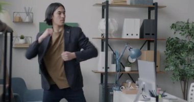 Asyalı iş adamı ofiste dans ediyor. Müzikle eğleniyor. Tatilin tadını çıkarıyor. Eğlence ve neşeli iş adamı konsepti.