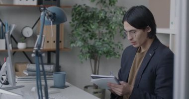 İş adamı deftere yazı yazıyor bilgisayar ekranına bakıyor ve ofiste kahve içiyor. Mesleki meslek ve işyeri kavramı.