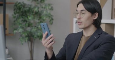 Asyalı iş adamı ofisteki akıllı telefonu kullanarak çevrimiçi video görüşmesi yapıyor. Sanal toplantı ve iş konferansı konsepti.