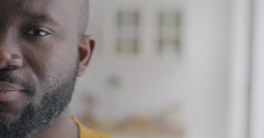 Afrika kökenli Amerikalı yarım suratlı bir adamın yavaş çekim portresi kameraya bakıyor ve bulanık arka planda gülümsüyor. İnsanlar ve olumlu duygu kavramı.