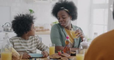 Anne oğluyla konuşurken küçük çocuk mutfakta anne ve babasıyla kahvaltı yapıyor. Aile ilişkisi ve sağlıklı beslenme konsepti.