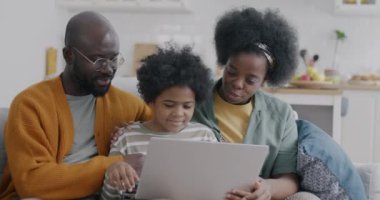 Küçük Afro-Amerikalı çocuk evde kanepede oturan anne ve babasıyla dizüstü bilgisayar kullanıyor. Çocukluk ve modern teknoloji kavramı.