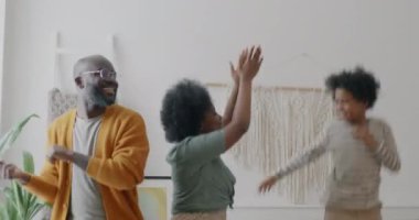Anne, baba ve çocuk evde boş vakitlerde müzik dinleyerek dans ediyorlar. Aile hayatı ve eğlence anlayışı.