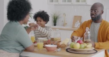 Afro-Amerikan mükemmel bir aile lezzetli, sağlıklı bir kahvaltı yapıyor. Mutfakta oturmuş, yemeğin tadını çıkarıyorlar. Ev hayatı ve beslenme konsepti.