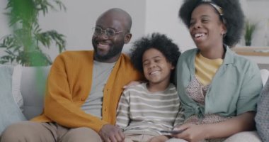 Neşeli Afro-Amerikan aile babası baba oğul TV seyrediyor ve gülüyor evdeki kanepede oturuyor. Kitle iletişim araçları ve eğlence konsepti.
