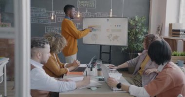 Afrika kökenli Amerikalı iş adamı çeşitli takımlar için sunum yapıyor. Ofiste konuşan elektronik kurulu işaret ediyor. İş ve insan kavramı.