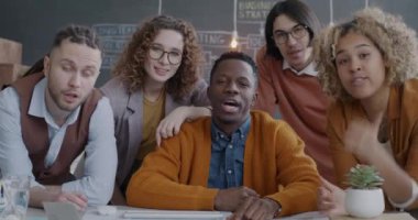 Çevrimiçi video görüşmesi yapan çeşitli işadamları grubu ofiste kameraya doğru başparmak göstererek konuşuyorlar. İletişim ve takım çalışması kavramı.