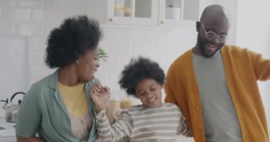 Neşeli Afro-Amerikan erkekleri kadın çocuk dansları müzik eşliğinde mutfakta eğleniyorlar. Aile hayatı ve eğlence anlayışı.