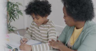 Oğlu evde defter yazarken, Afrikalı Amerikalı bir kadın çocuklara çalışmalarında yardım ediyor. Eğitim ve aile yaşam tarzı kavramı.