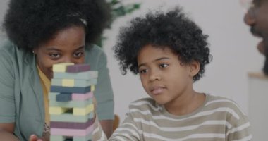 Neşeli Afrikalı Amerikalı çocuk, anne ve babasıyla oynuyor evdeki ahşap tuğlalardan kule inşa ediyor. Oyun ve aile yaşam tarzı kavramı.