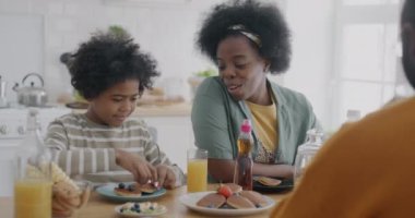 Küçük çocuk, anne ve babasıyla kahvaltı yapıyor kreplere akçaağaç pekmezi döküyor ve evde yemeğin tadını çıkarıyor. Aile ve beslenme konsepti.