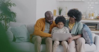 Neşeli Afro-Amerikan aile babası ve çocuğu dizüstü bilgisayar kullanıyorlar ve evdeki kanepede gülüyorlar. Modern teknoloji ve yaşam tarzı kavramı.