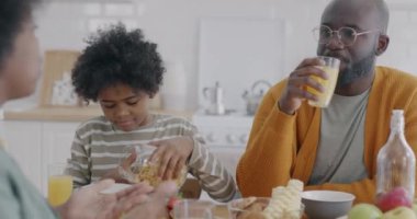 Afro-Amerikan çocuk, anne ve babasıyla kahvaltı yapıyor. Lezzetli sağlıklı yemekler yiyor. Mutfaktaki yemeğin tadını çıkarıyor. Ev hayatı ve insan konsepti.