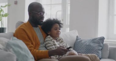 Baba ve oğul Afro-Amerikan bir aile televizyon seyrediyor. Gülüyorlar, koltukta oturuyorlar. Kitle iletişim araçları ve eğlence konsepti.
