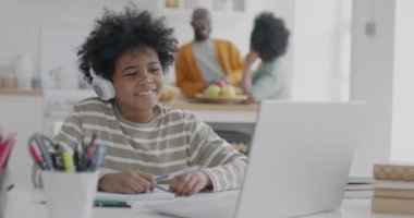 Annesi ve babası mutfakta konuşurken, Afrikalı Amerikalı çocuk internette bilgisayar başında sanal öğretmenle konuşuyor. İnternet eğitimi ve çocukluk kavramı.