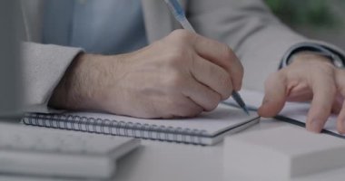 İş adamı ofiste masa başında çalışırken, erkek ellerinin deftere yazı yazması. İş planlaması ve mesleki işgal kavramı.