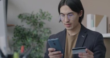 Akıllı telefon ve kredi kartı kullanan Asyalı işadamı, ofisteki elektronik ticaret ve finans mobil uygulamalarına odaklandı. İş ve para kavramı.