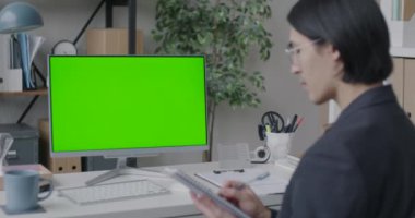 Not defterine yazan Asyalı işadamı ofiste krom anahtar yeşil ekranlı bilgisayara bakıyor. Modern teknoloji ve iş kavramı.