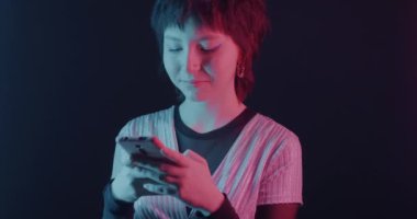 Asyalı bir kadın siyah arka planda neon ışıkta akıllı telefon kullanarak sesli mesaj kaydediyor. İletişim ve aygıt kavramı.