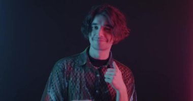 Neon ışıkta konfeti düşüşünü izleyen genç bir adamın ağır çekimde dans etmesi. Özel durum ve festival konsepti.