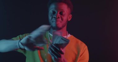 Zengin Afro-Amerikan bir adamın karanlık arka planda neon ışığı altında dans edişinin portresi. Finans ve zengin kişi kavramı.