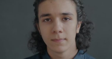 Gri stüdyo arka planındaki kameraya bakan sakin İspanyol adamın yavaş çekim portresi. Yüz ifadesi ve bireysel biçim kavramı.