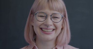 Siyah arka planda kameraya bakıp gülen neşeli genç bir kadının yavaş çekim portresi. Pozitif duygu ve mutlu insanlar konsepti.