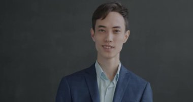 Siyah arka plandaki kameraya gülümseyen takım elbiseli genç adamın yavaş çekim portresi. İnsanlar ve Merhaba sembol kavramı.