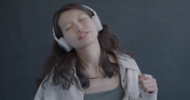 Kaygısız Asyalı kadın siyah arka planda dans eden kulaklıklarla müzik dinliyor. Mutlu insan ve modern teknoloji kavramı.