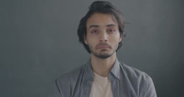 Mutsuz Orta Doğulu bir adamın portresi gri arka planda baş parmak hareketi gösteriyor. Hayal kırıklığı ifadesi ve insanların kavramı.