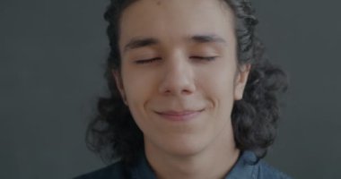 Gri arka planda kameraya gülümseyen mutlu İspanyol adamın yavaş çekim portresi. İnsanlar ve olumlu duygu kavramı.