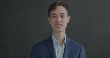 Takım elbiseli mutlu genç adamın yavaş çekim portresi siyah stüdyo arka planında gülümseyen el hareketlerini gösteriyor. İnsanlar ve memnuniyet işareti kavramı.