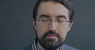 Gözlüklü Orta Doğulu özgüvenli bir adamın yavaş çekim portresi siyah stüdyo arkaplanındaki kameraya bakıyor. İnsanlar ve yüz ifadesi kavramı.