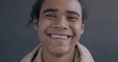 Siyah arka planda kameraya bakıp gülen Afro-Amerikan bir adamın yavaş çekim portresi. Mutlu insanlar ve olumlu duygu kavramı.
