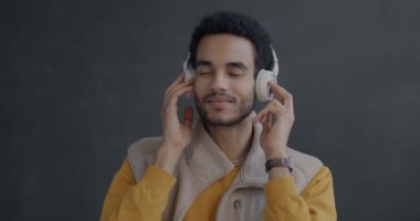 Siyah stüdyo arka planında dans eden, kulaklıkla müzik dinleyen kaygısız Afrikalı Amerikalı adamın portresi. İnsanlar ve eğlence konsepti.