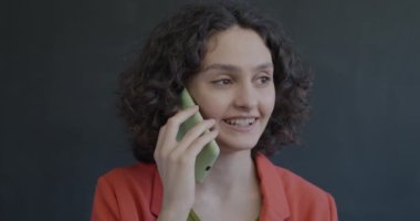 Cep telefonuyla konuşan neşeli genç bir kadın siyah arka planda gülüyor. Cep telefonu iletişimi ve mutlu insan kavramı.
