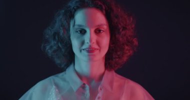 Havadan öpücük gönderen ve karanlık arka planda neon ışıkta gülümseyen çekici genç bir kadının portresi. İnsanlar ve ilişki kavramı.