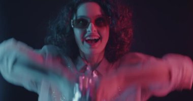 Konfeti atan ve dans eden mutlu genç bir kadın karanlık arka planda neon ışıkta eğleniyor. Eğlence ve şenlik havası..