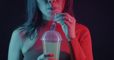 İsimsiz bir kadın kokteyl içiyor ve karanlık arka planda neon ışıkta gülümsüyor. İçecek ve gece hayatı kavramı.